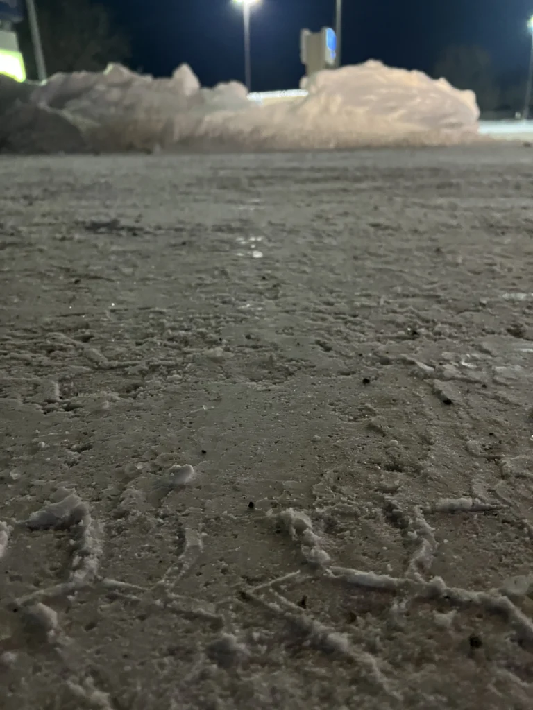 Snow-covered surface with icy patches and snow piles, illustrating the need for effective snow removal services for HOAs in Sioux Falls, SD.