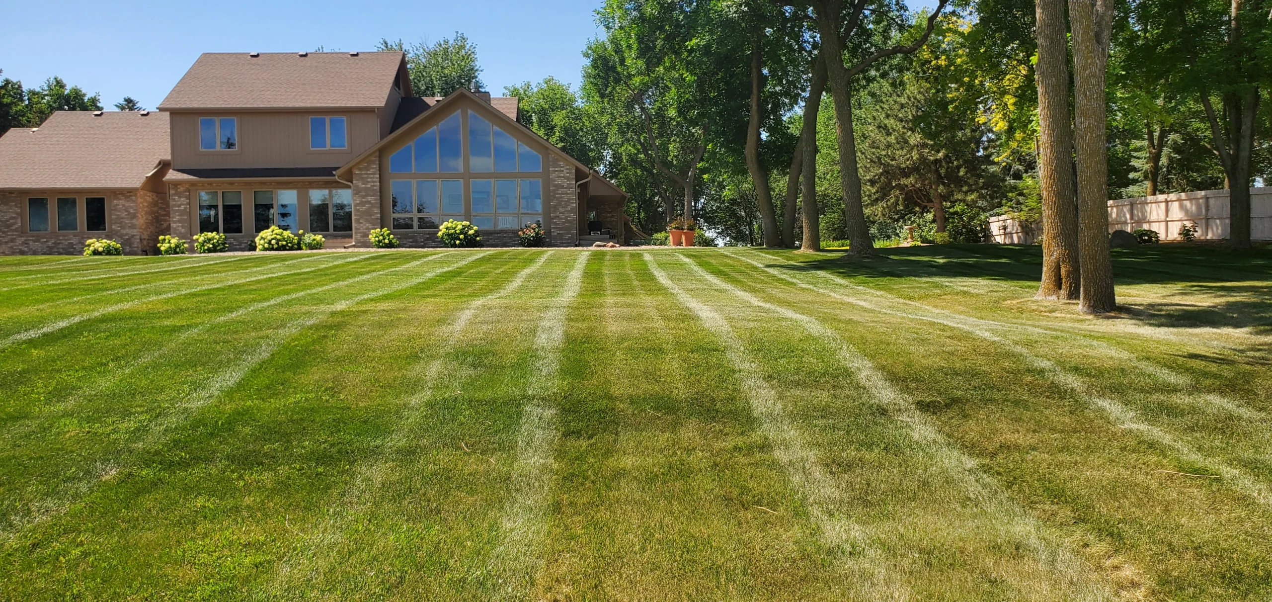 Lush green lawn with professional mowing stripes, showcasing a well-maintained residential property in Sioux Falls, SD, emphasizing the quality of lawn care services by Next Level Outdoor Services.
