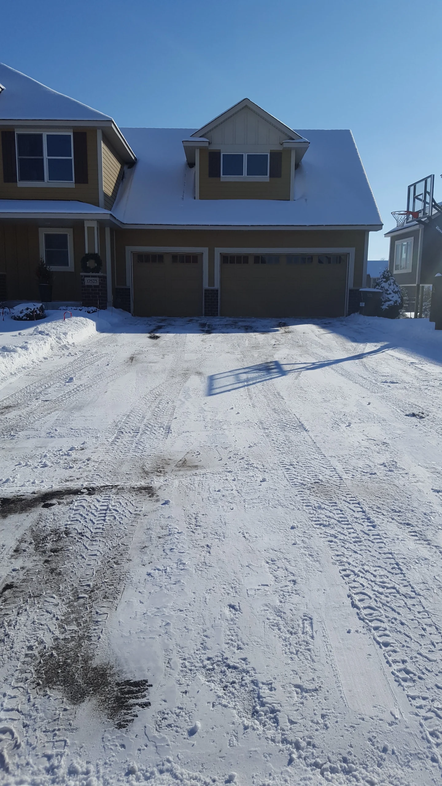 Residential driveway cleared of snow, showcasing effective snow removal services by Next Level Outdoor Services in Sioux Falls, SD, with clear tire tracks and a snow-covered landscape.