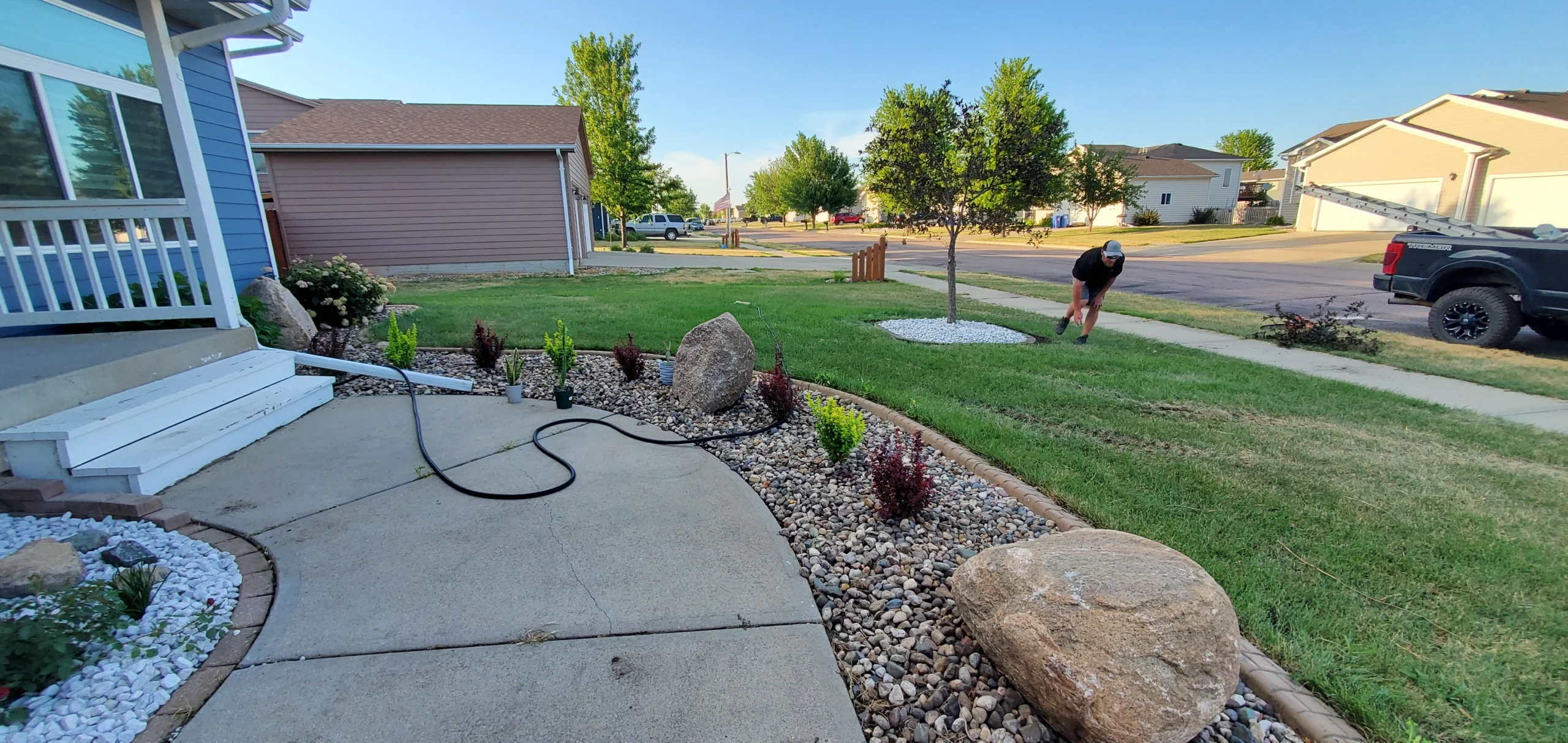 Landscaper working on decorative stone installation in residential yard, featuring a variety of plants and rocks, enhancing curb appeal for Sioux Falls homeowners.
