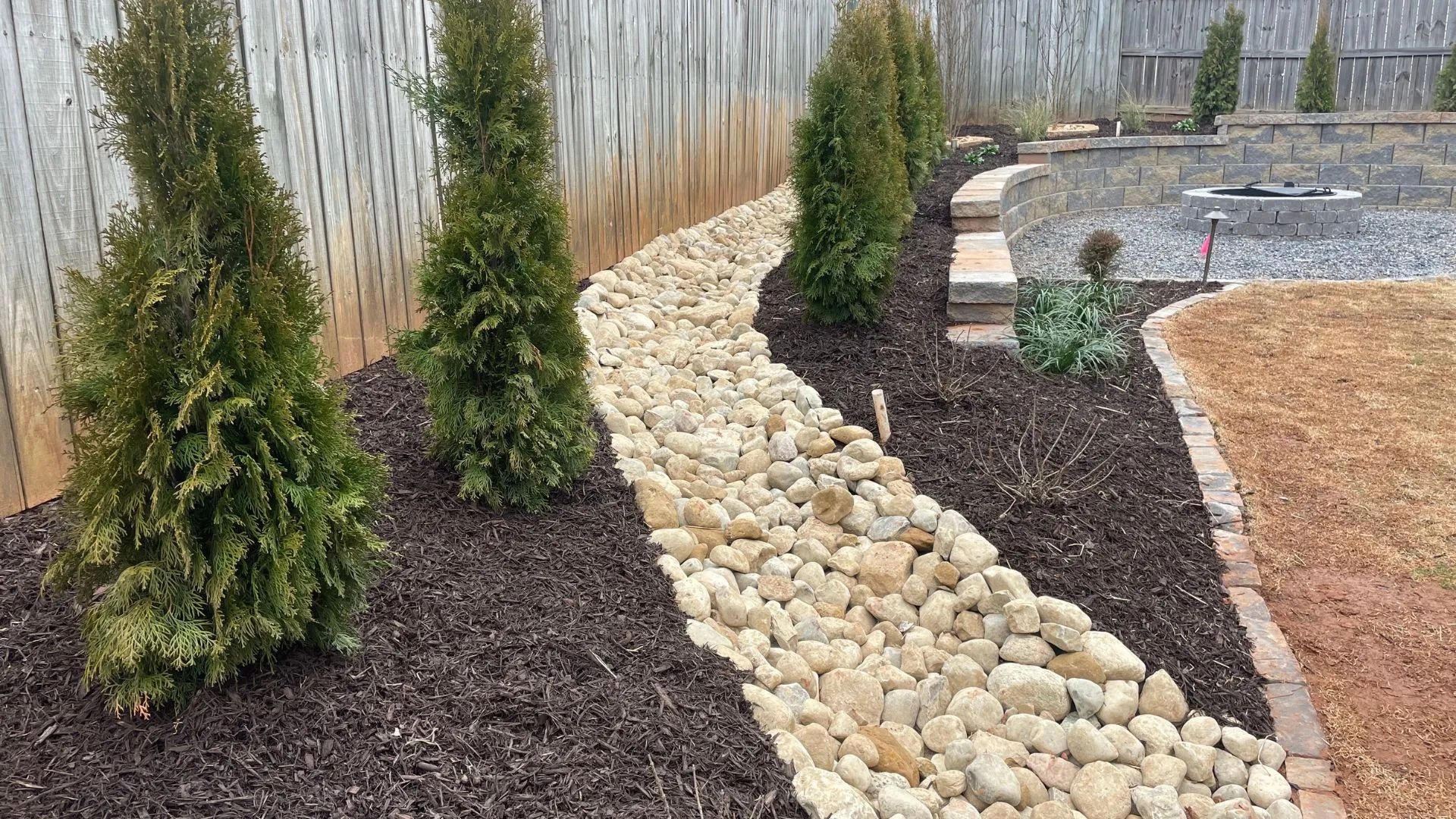 Landscaped pathway featuring river rocks bordered by evergreen shrubs and mulch, illustrating effective drainage solutions for outdoor spaces in Sioux Falls.