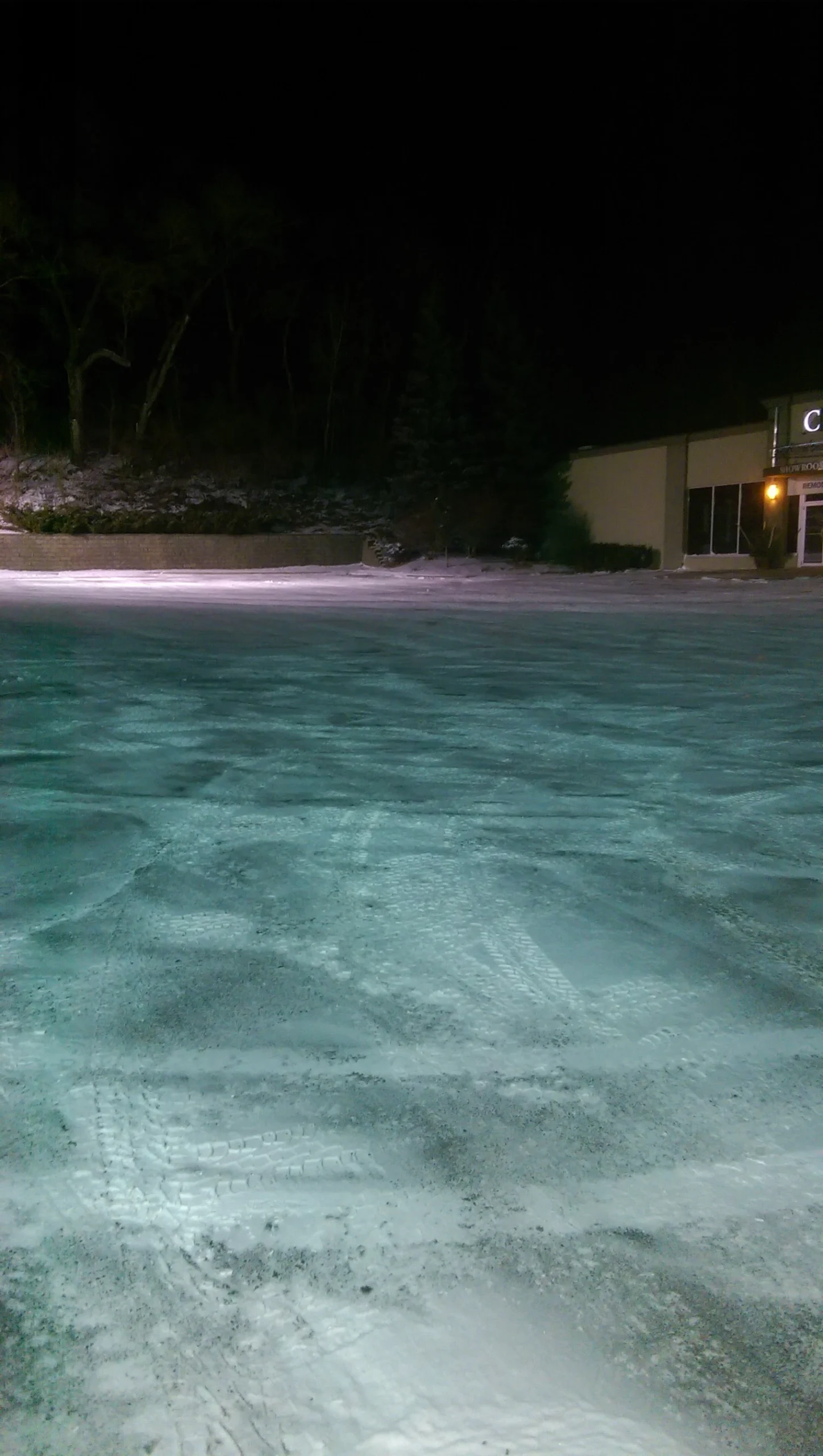 Snow-covered parking lot at night with tire tracks, showcasing ice management services by Next Level Outdoor Services in Sioux Falls, SD.